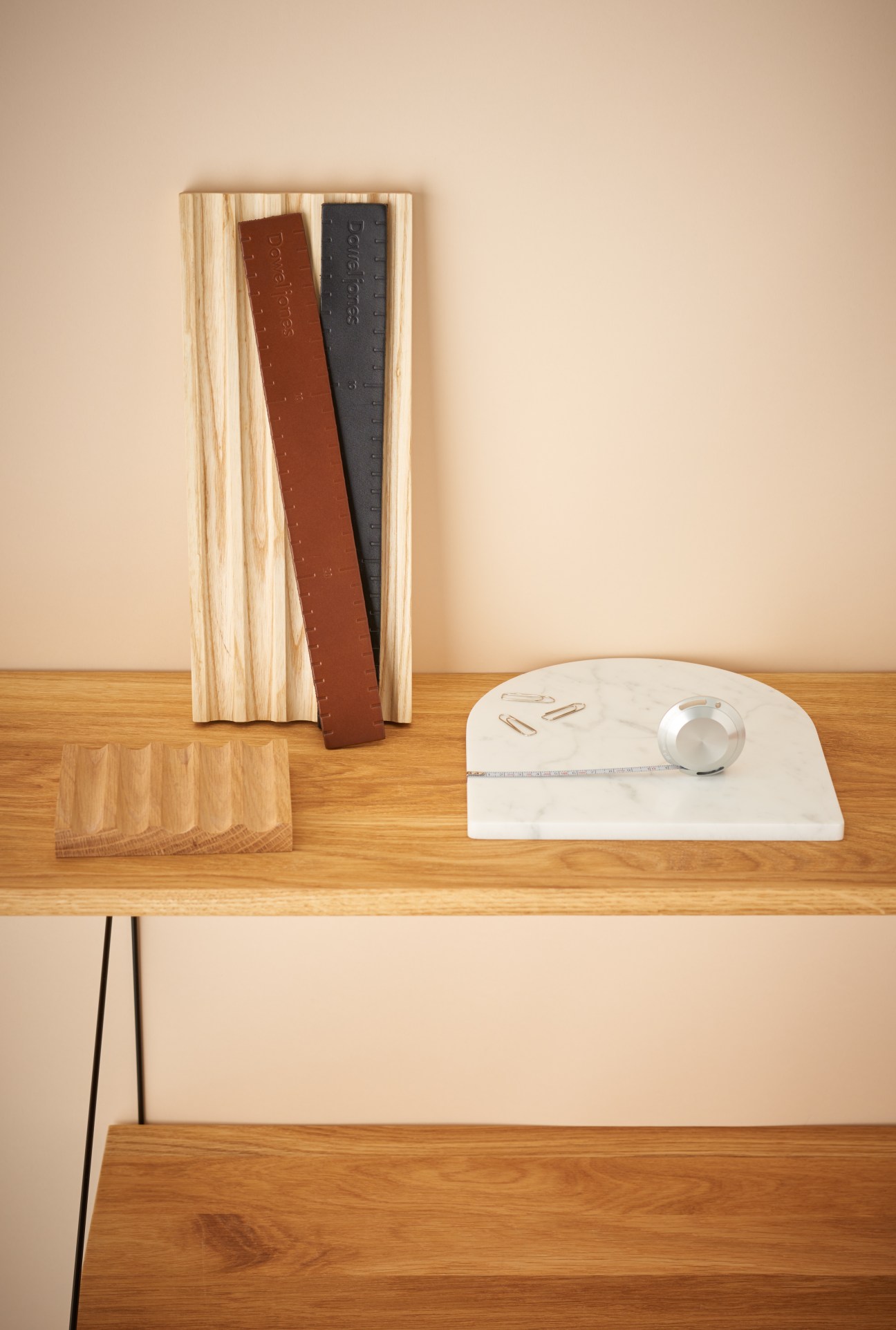 Desk accessories including a wooden ruler holder with brown and black leather, a white marble tape measure holder, and metal paper clips arranged on a wood shelf.