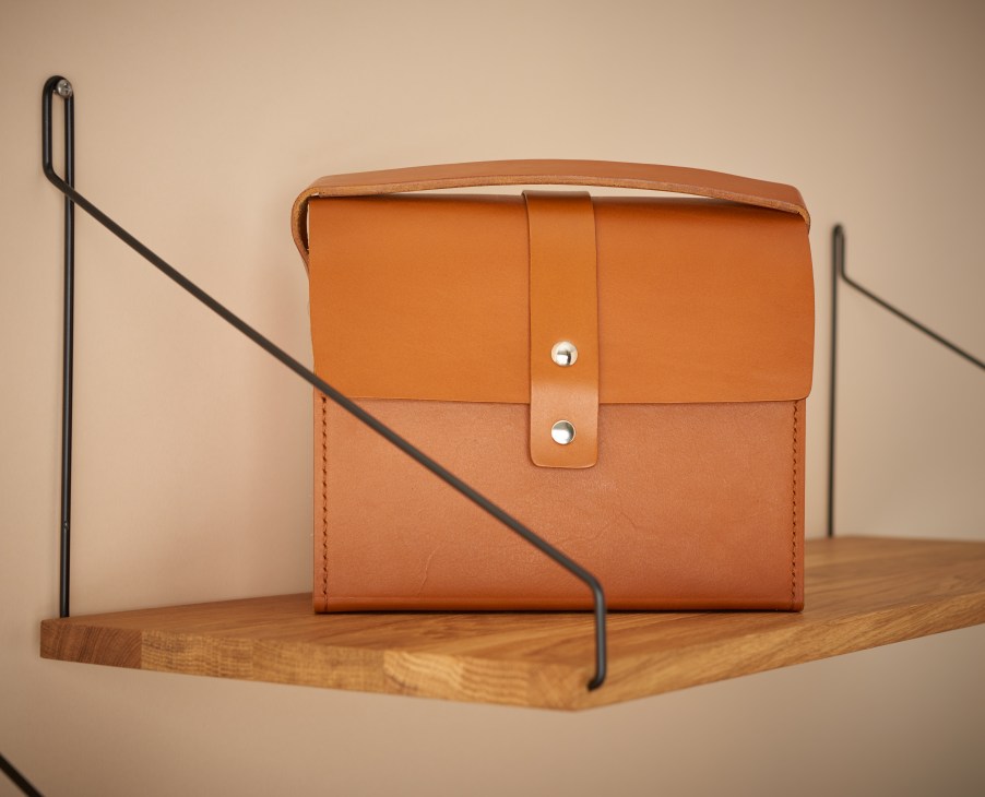 Tan leather shaving bag with metal clasps displayed on wooden base.