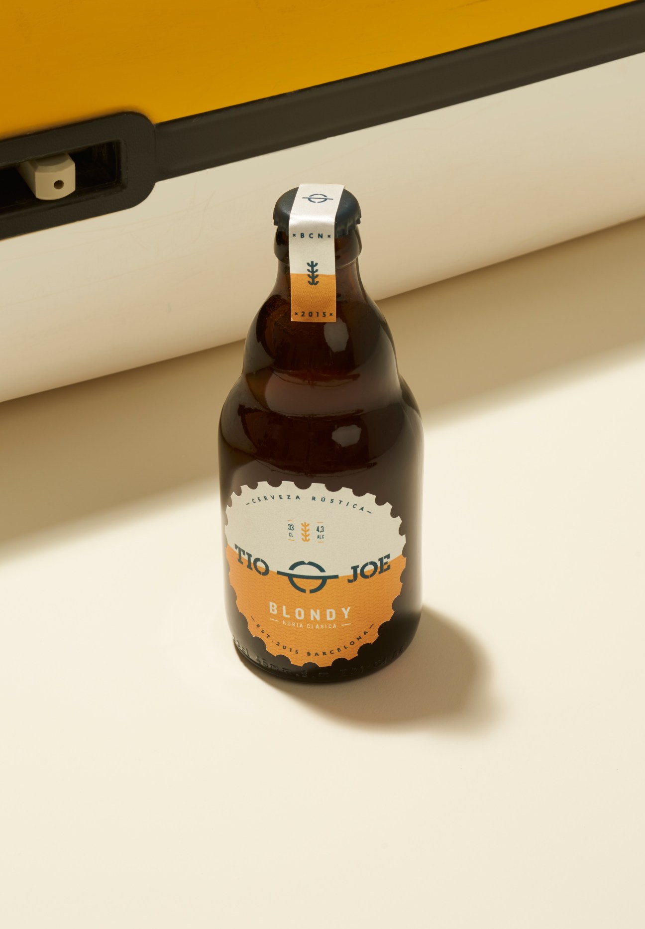 Tio Joe Blondy craft beer bottle with rippled logo and cog-shaped label on neutral background.