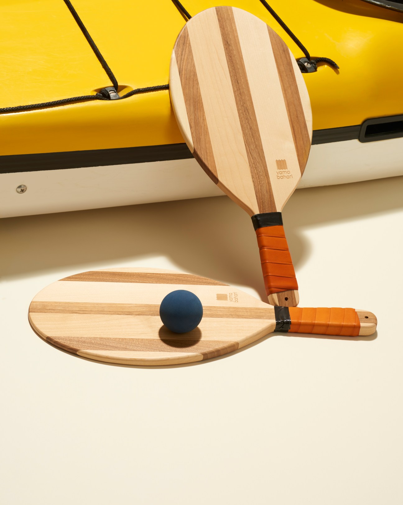 Yamabahari beach bats made from American walnut and beech wood with orange leather-wrapped handles displayed against a yellow background.