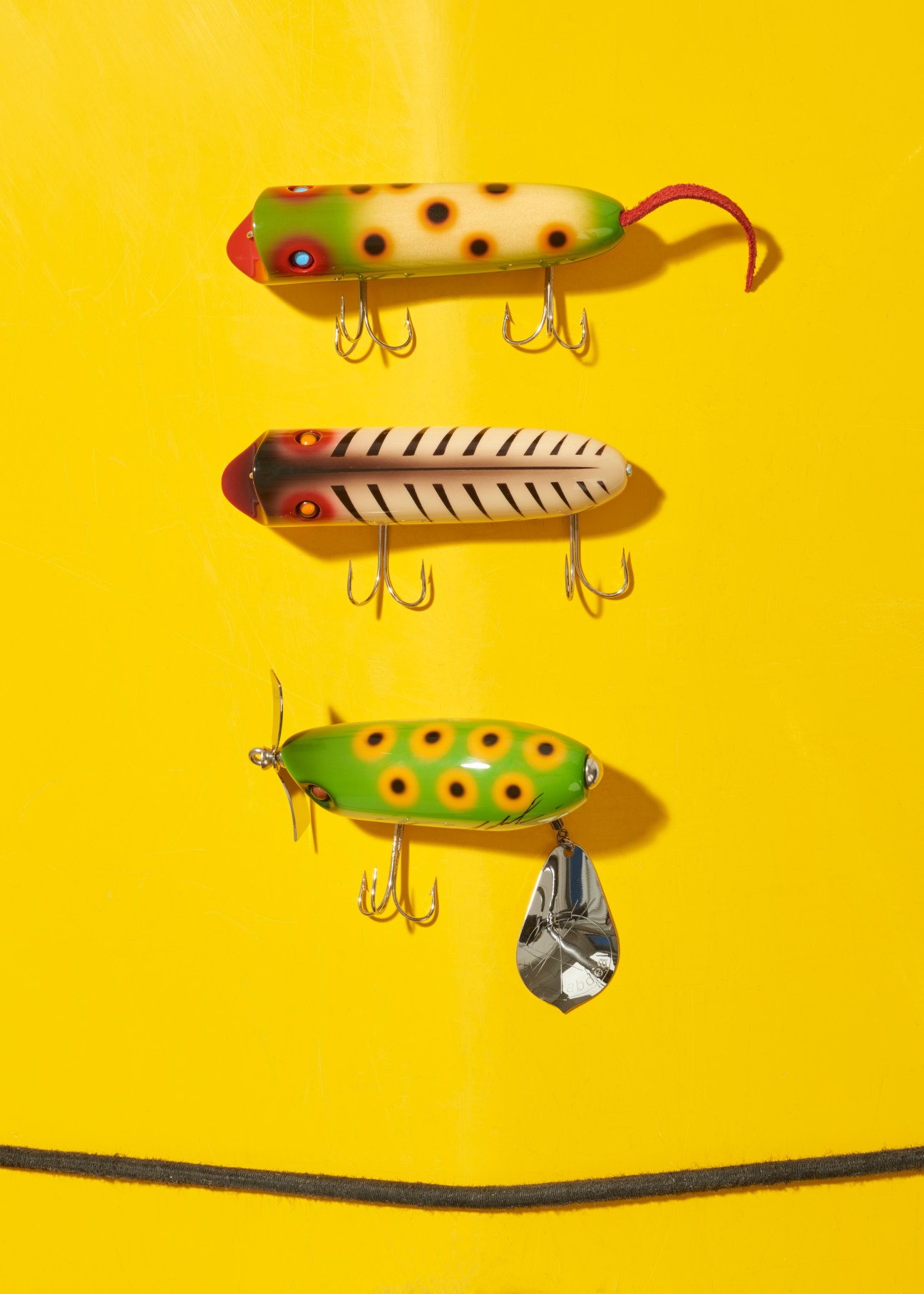Three colorful handmade wooden fishing lures with hooks displayed on a yellow background.
