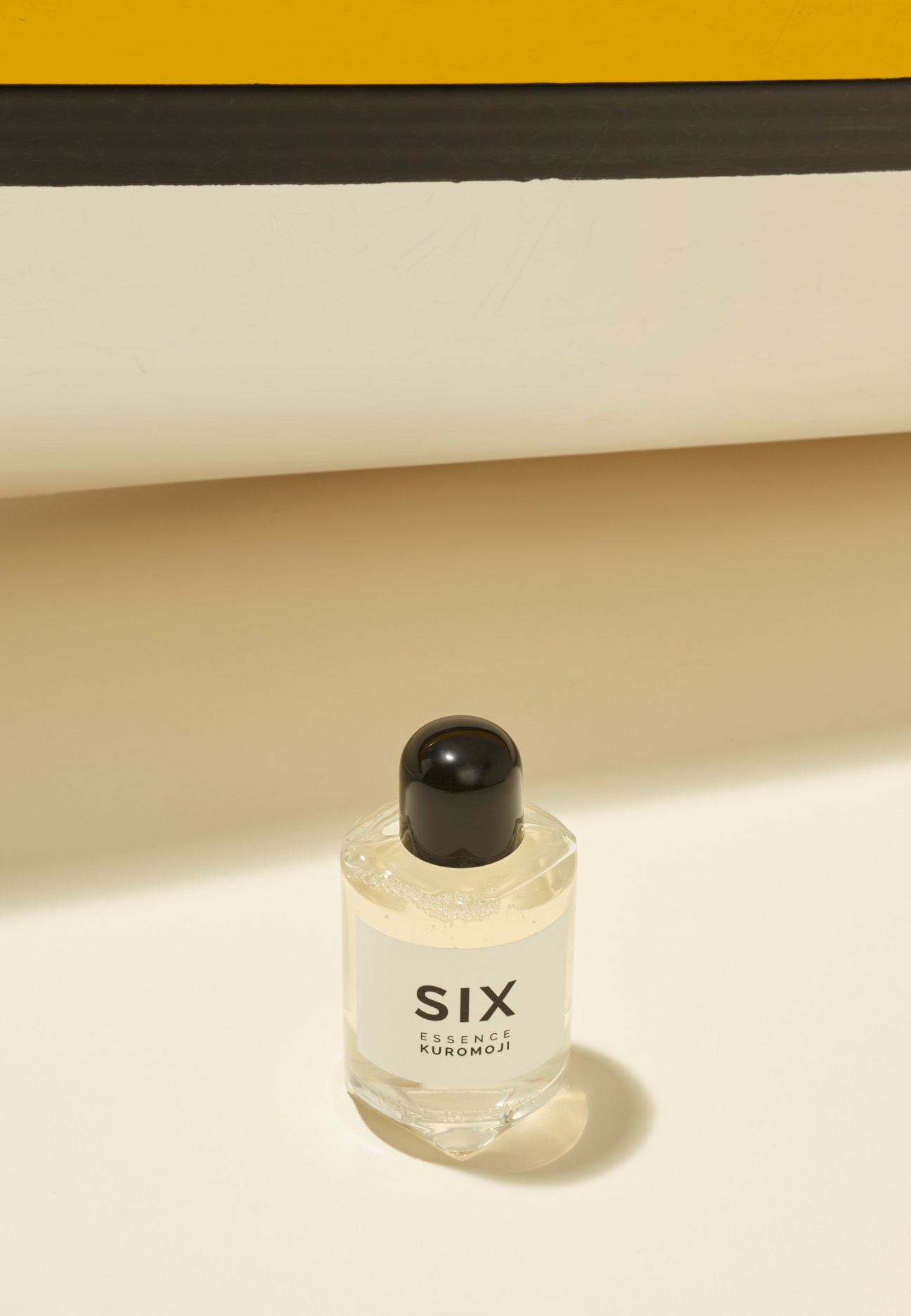 Six Essence Kuromoji cosmetic product in a clear glass bottle with black cap on beige background.