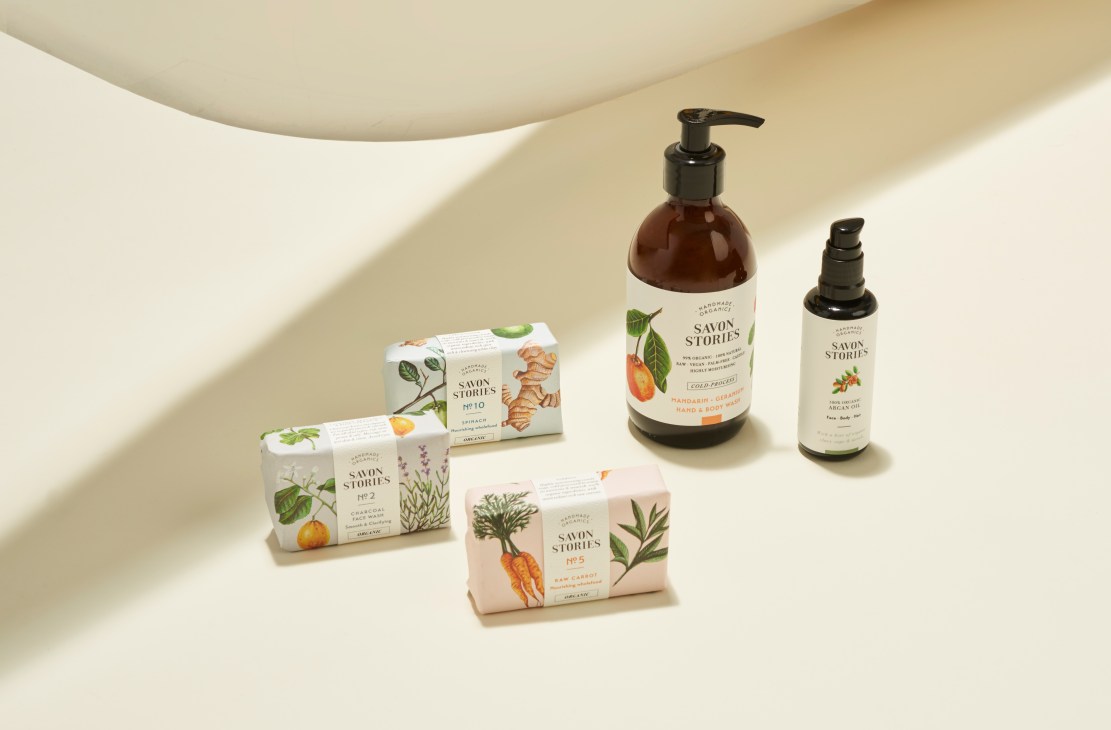 Savon Stories soap bars and oils displayed on a neutral surface with botanical illustrations on packaging.