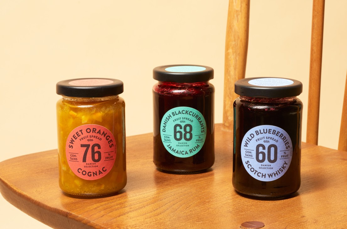 Three jars of Danish Selection jam with colorful circular labels on a wooden surface against a cream background.