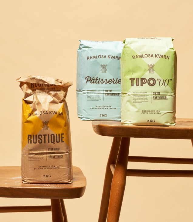 Three bags of Ramlösa Kvarn flour in different varieties displayed on wooden stools against a beige background.