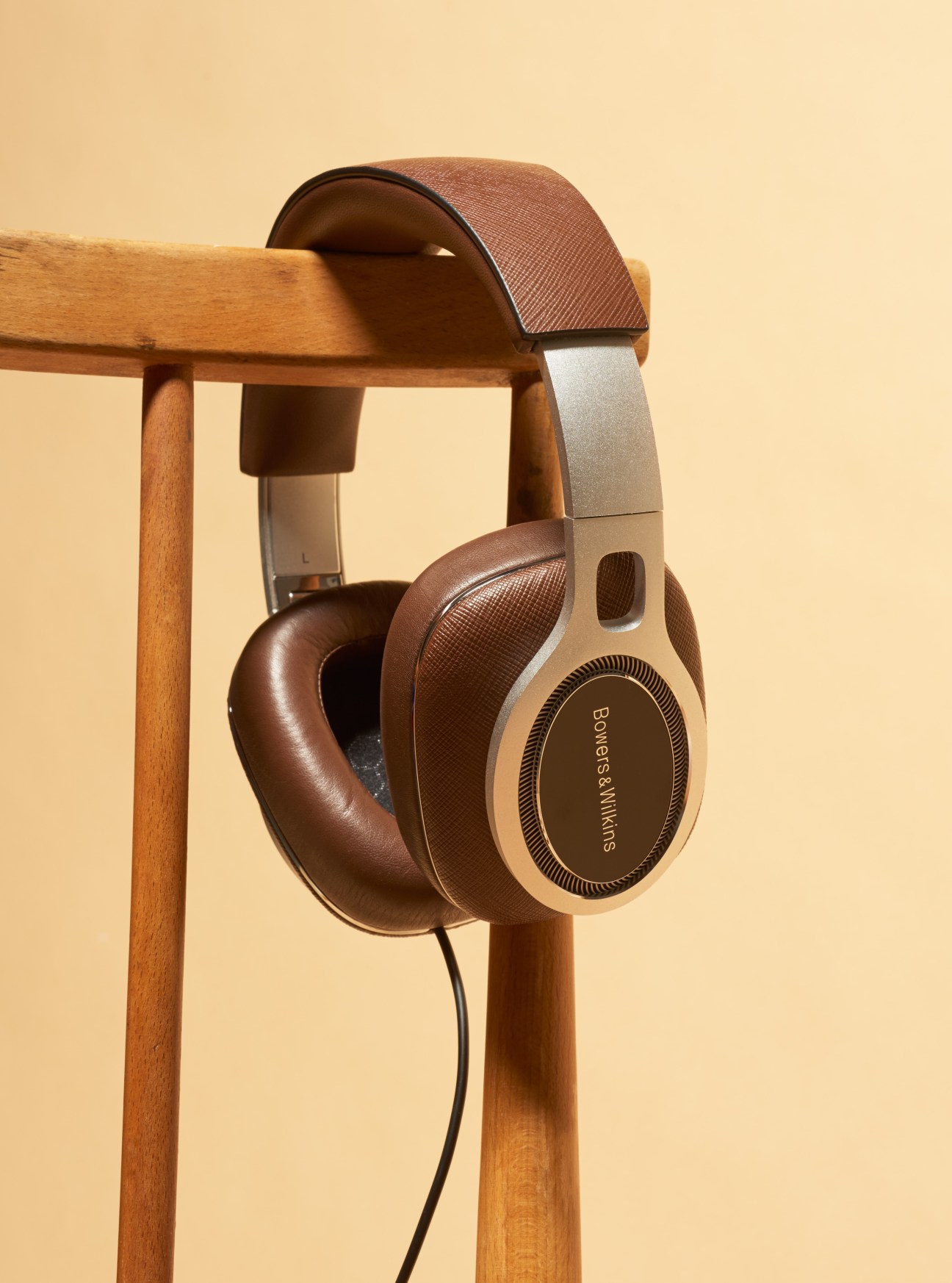 Bowers & Wilkins P9 Signature headphones with brown Saffiano-leather trim and memory foam ear-pads displayed on wooden stand.