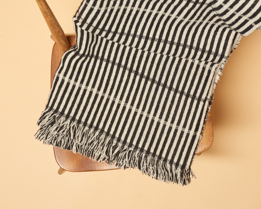 Black and cream striped wool throw with fringe draped over wooden chair against beige background