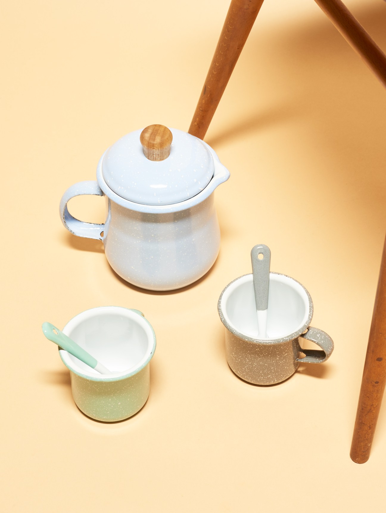 Colorful enamelware set by Criolla including a light blue pot with wooden handle, and two smaller cups in mint and taupe with matching spoons.