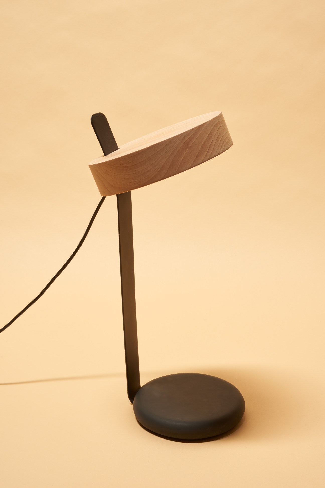 Wooden desk lamp with curved wood diffuser and dark metal base by Saif Faisal.