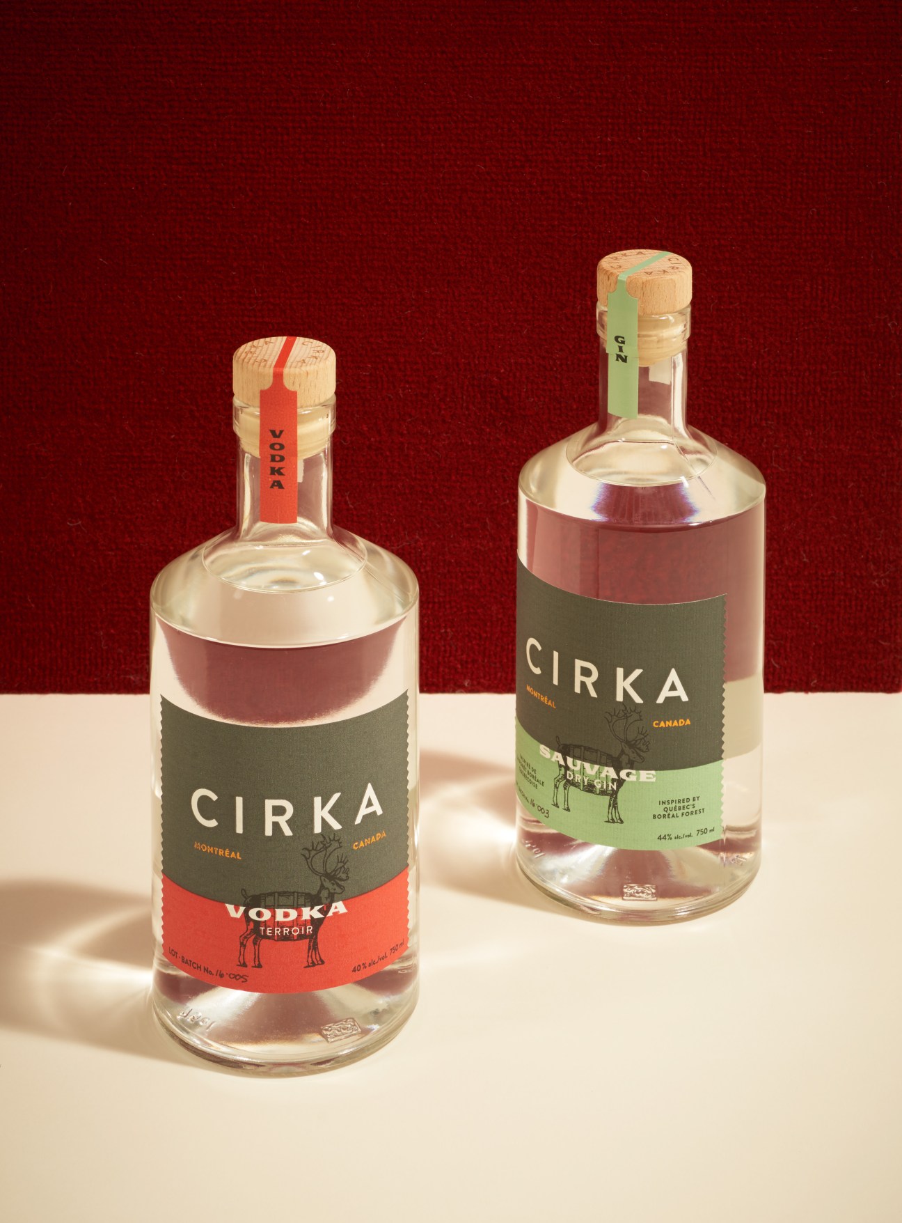 Two Cirka spirit bottles with clear liquids, one vodka and one gin, against a red background