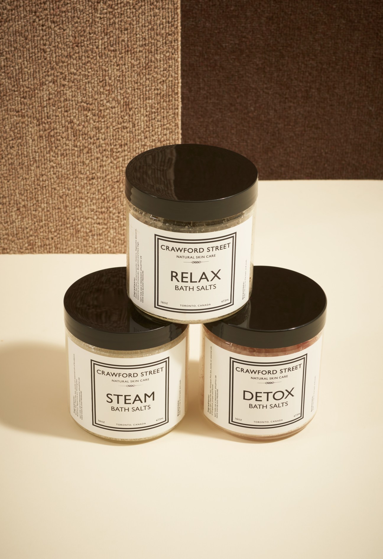 Three Crawford Street bath salt jars with black lids in Relax, Steam and Detox varieties stacked on neutral surface