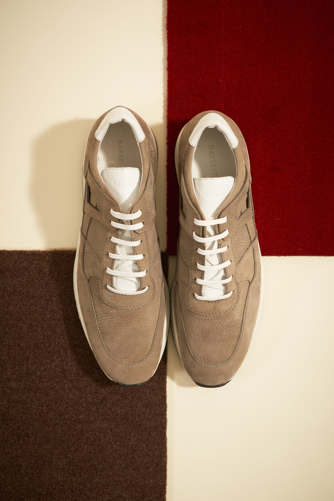 A pair of beige Darzé Studios leather trainers with white laces on a color-blocked surface