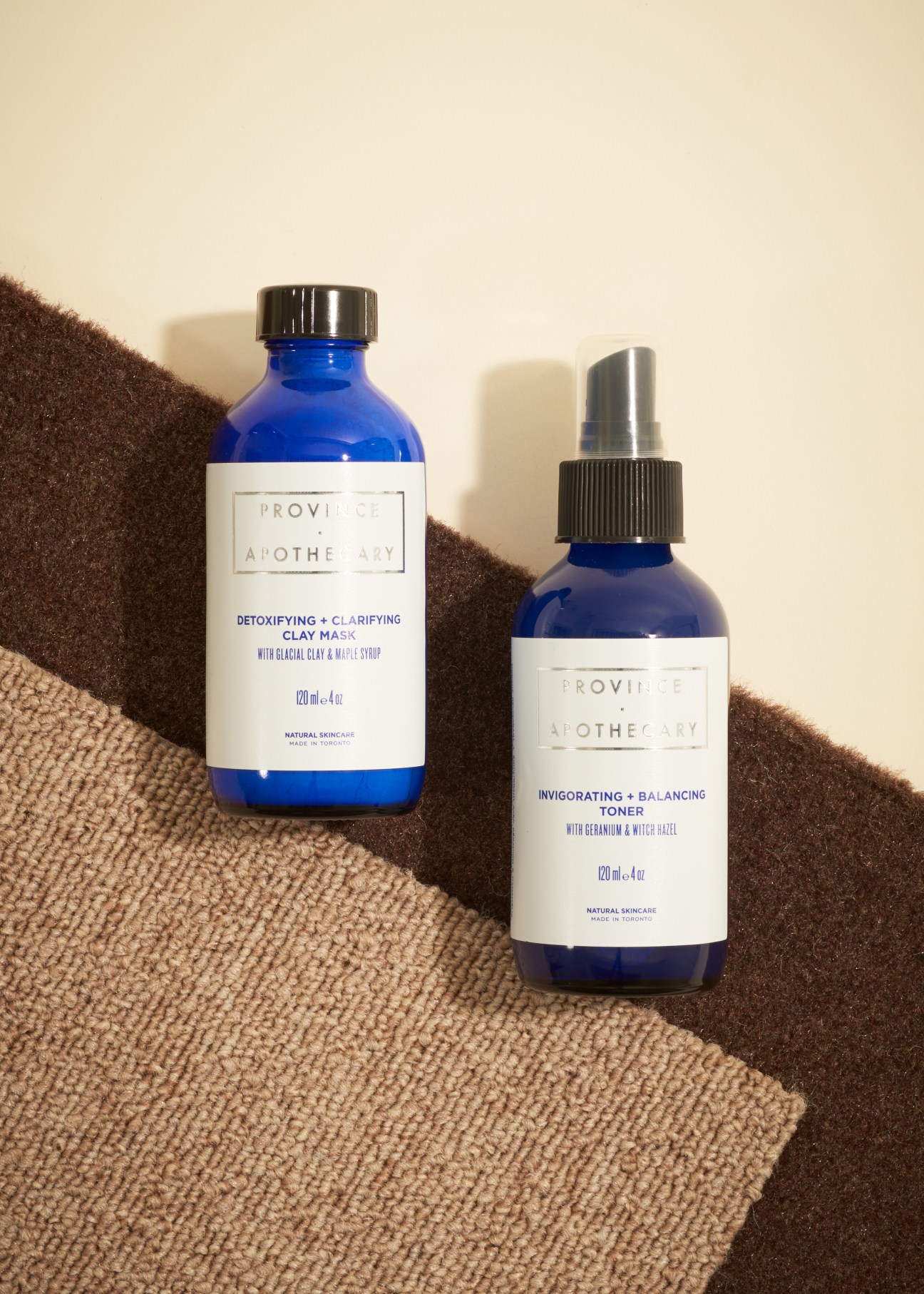 Two blue glass bottles of Province Apothecary skincare products on textured surface with dramatic shadows