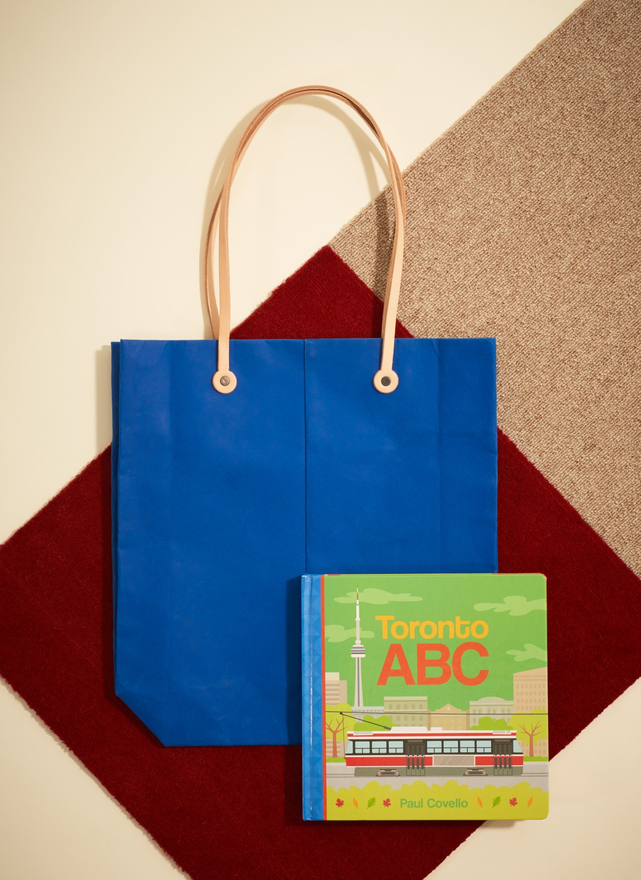 Blue tote bag with leather handles next to Toronto ABC children's book