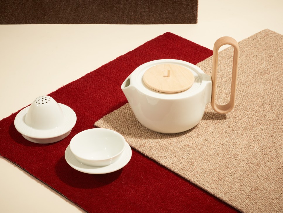 White porcelain tea set with teapot, cups, and filter arranged on red and beige textured mats