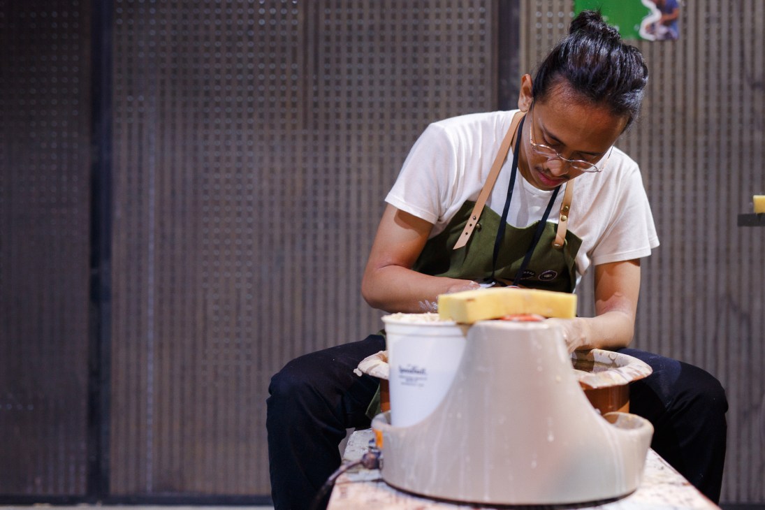 Person working at pottery wheel in workshop space with corrugated metal walls.