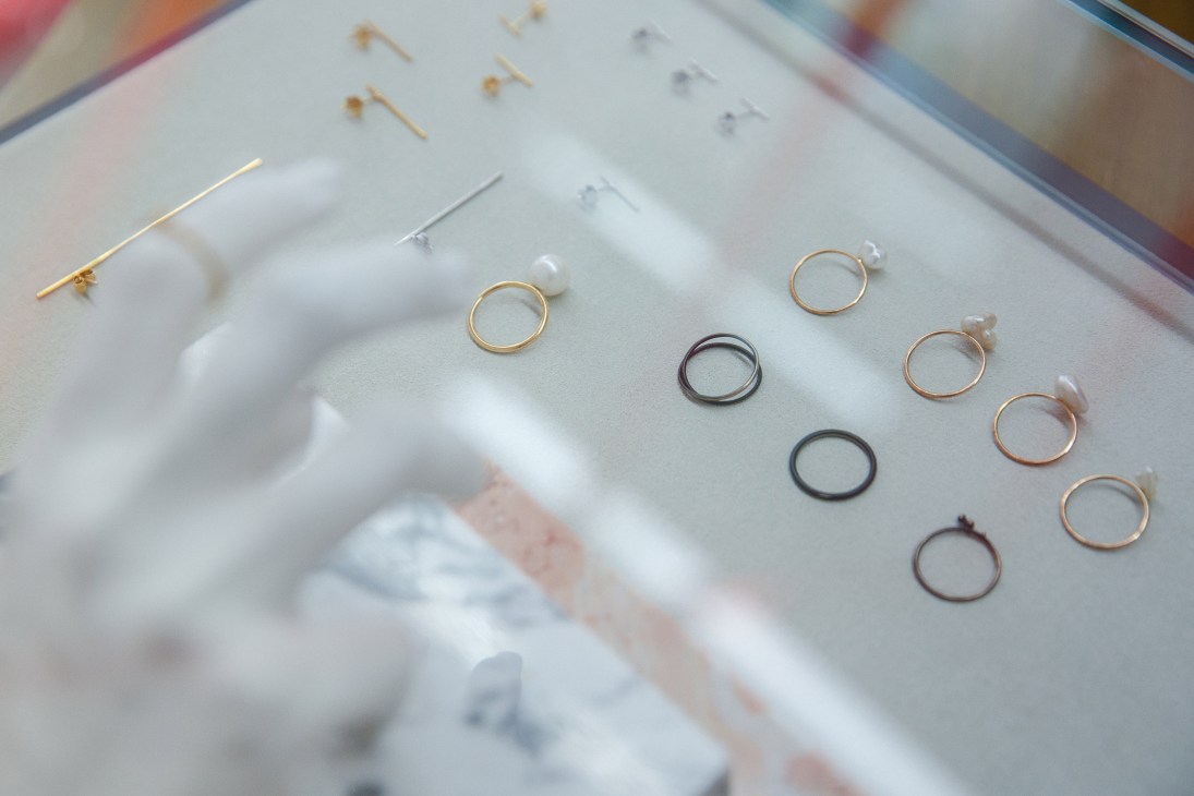 Display of delicate jewelry rings in gold, rose gold, and dark metal finishes on a white surface.