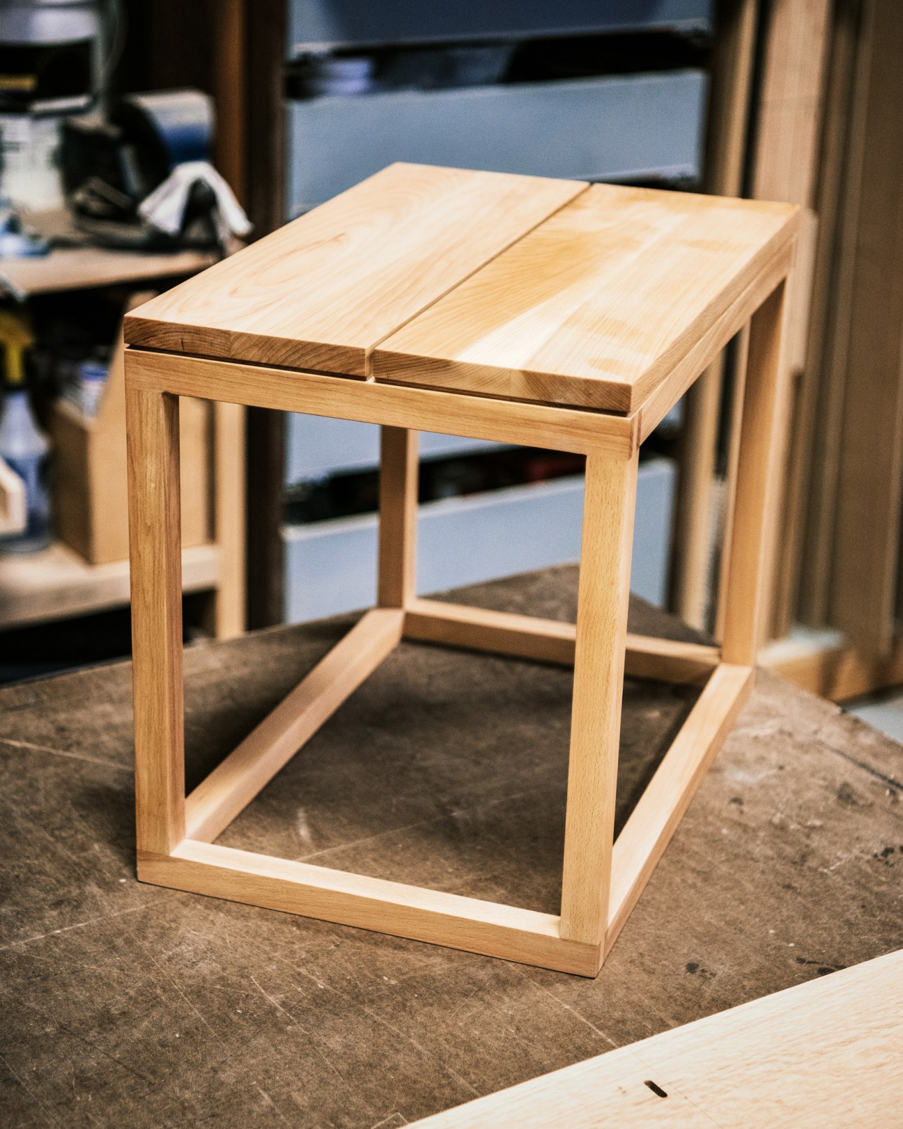 Light wood stool with clean lines and geometric frame design in a workshop setting.