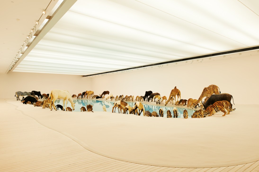 Cai Guo-Qiang's 'Heritage' installation featuring 99 life-like animal sculptures gathered around a crystal-clear watering hole in a gallery space.
