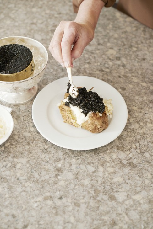 Hand spooning American Transmontanus caviar onto crème fraîche and baked potato.