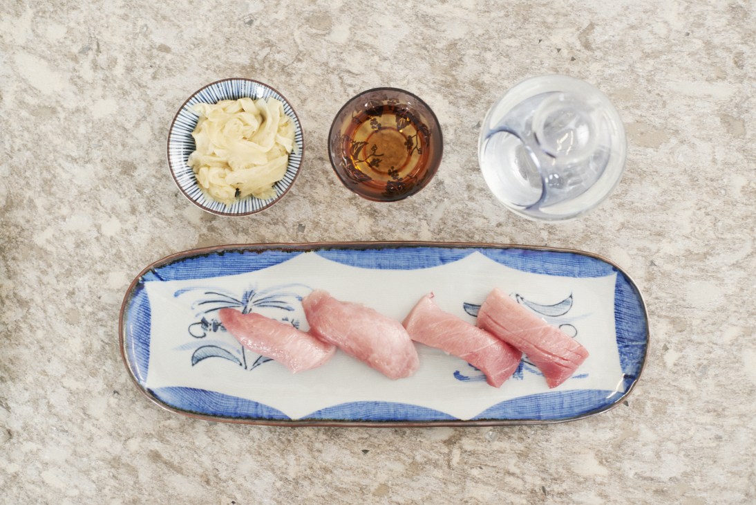 Four pieces of nigiri sushi with pink fish on a blue and white ceramic plate with ingredients in bowls above.