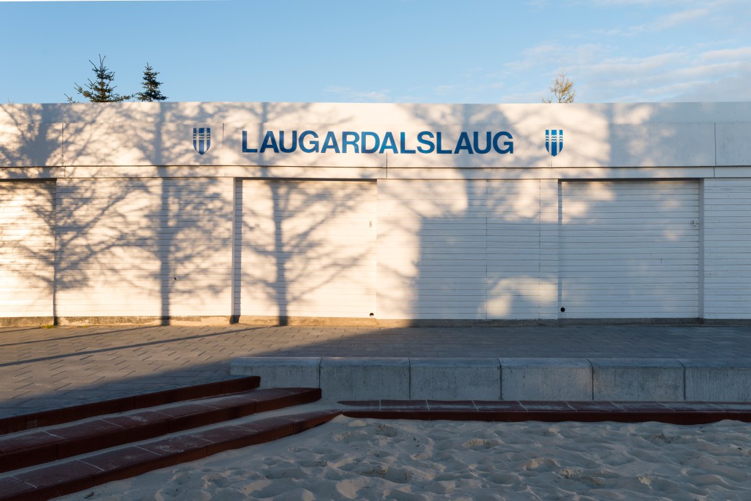 Exterior of Laugardalslaug swimming pool in Reykjavik with white concrete building and signage.
