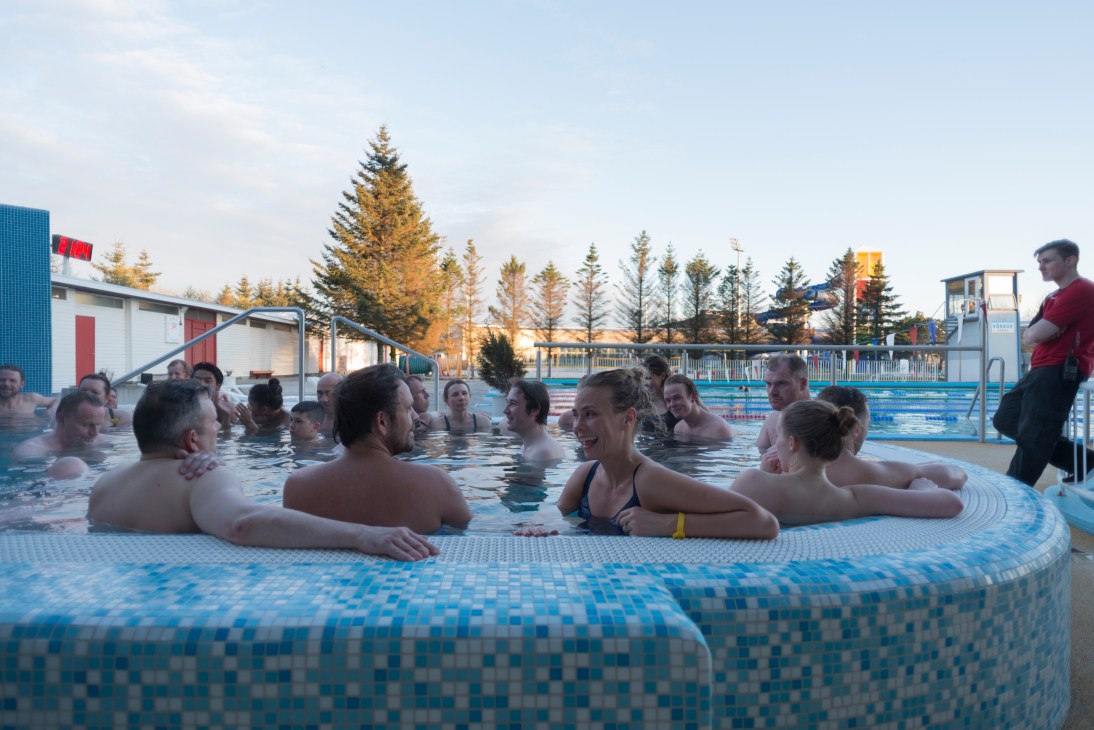Multiple swimmers relaxing in a large outdoor hot tub at Laugardalslaug in Iceland at dusk.
