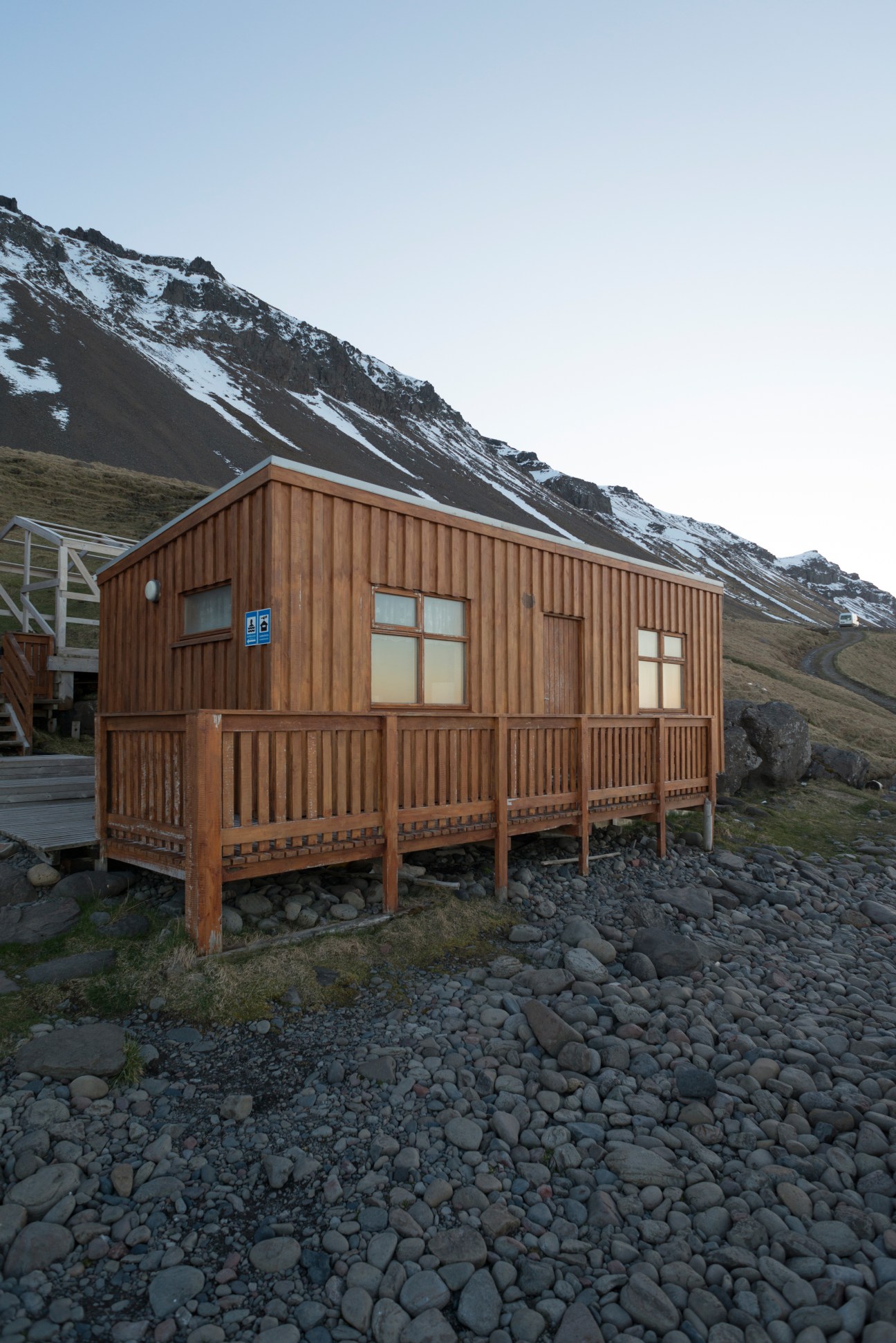 Brown wooden summerhouse with pitched roof beside snow-capped mountain in Iceland.