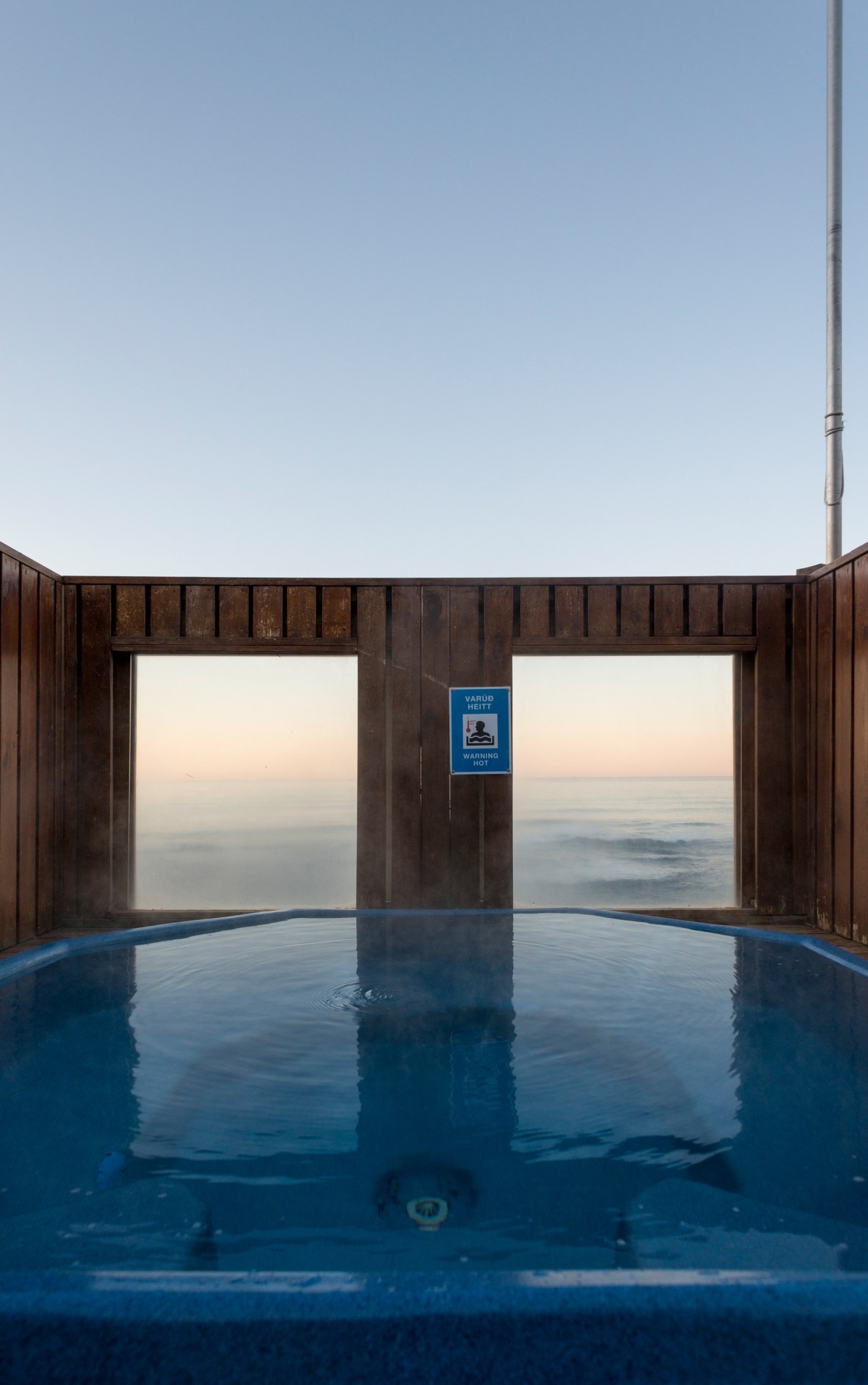 View from inside a geothermal hot tub with wooden walls framing a calm sea horizon at dusk in Iceland.