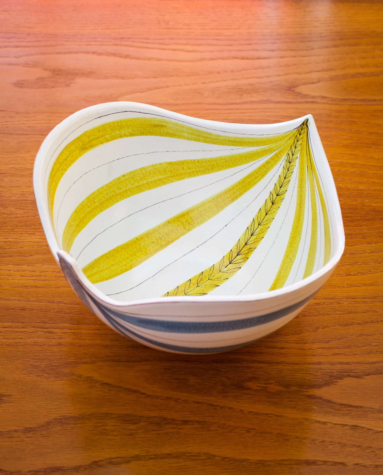 Stig Lindberg's 1950s ceramic bowl with yellow striped pattern on wooden surface.