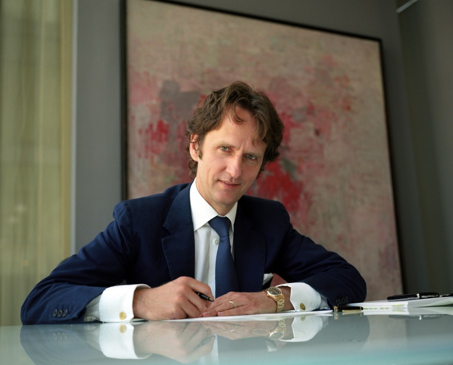 Tobias Meyer, worldwide head of contemporary art at Sotheby's, seated at a desk wearing a navy suit and blue tie.