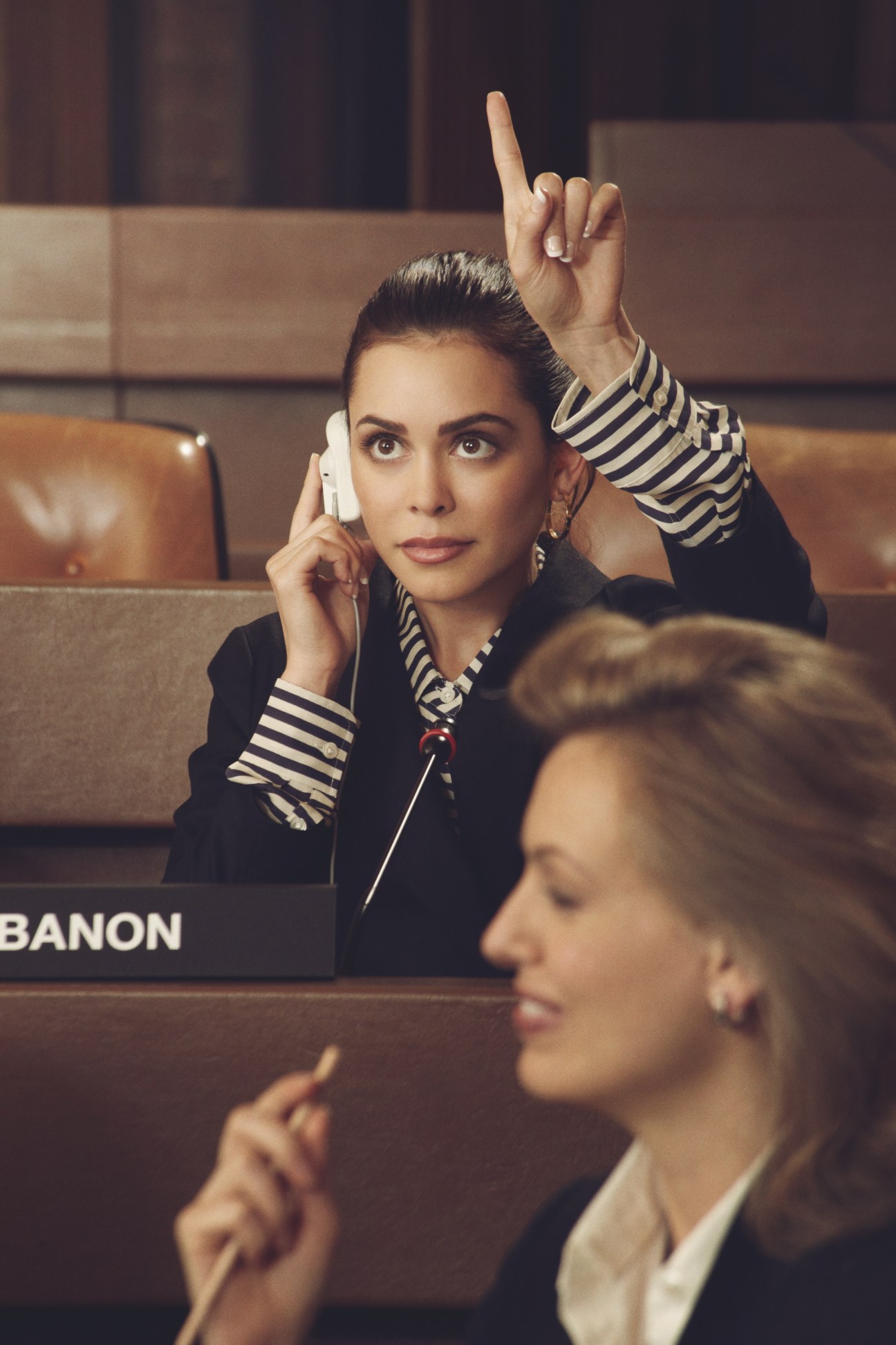 Female delegate representing Lebanon in striped blazer with headphones, raising hand at UN assembly.