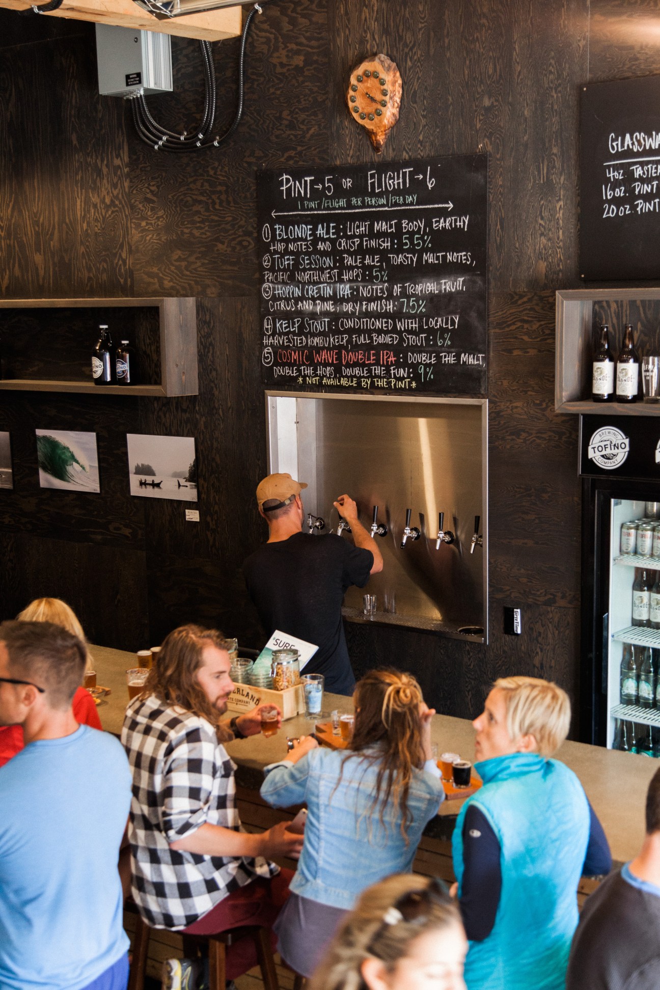 Bartender pouring beer at Tofino Brewing with chalkboard menu showing beer flight options