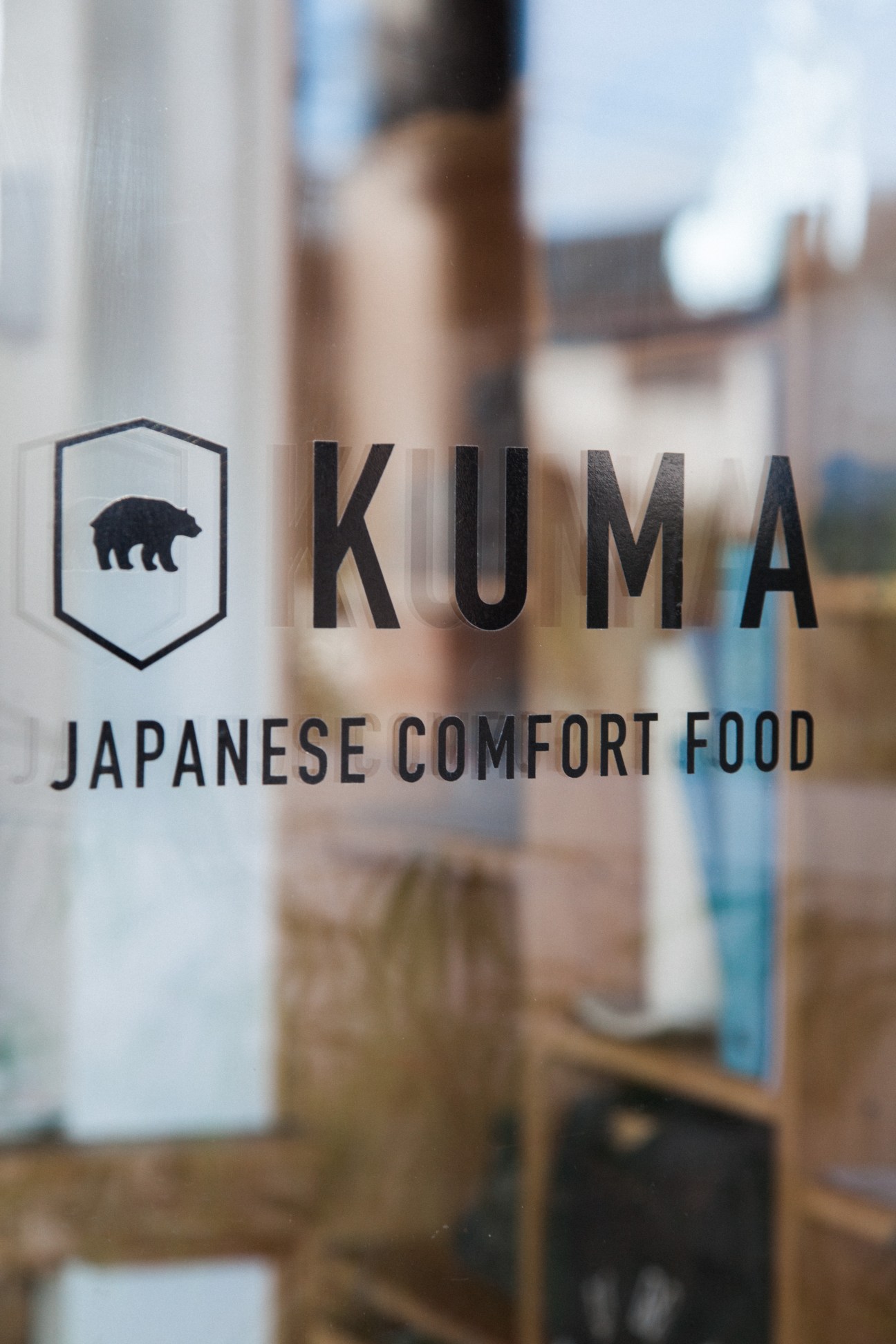Glass window with Kuma Japanese Comfort Food logo and text in black lettering