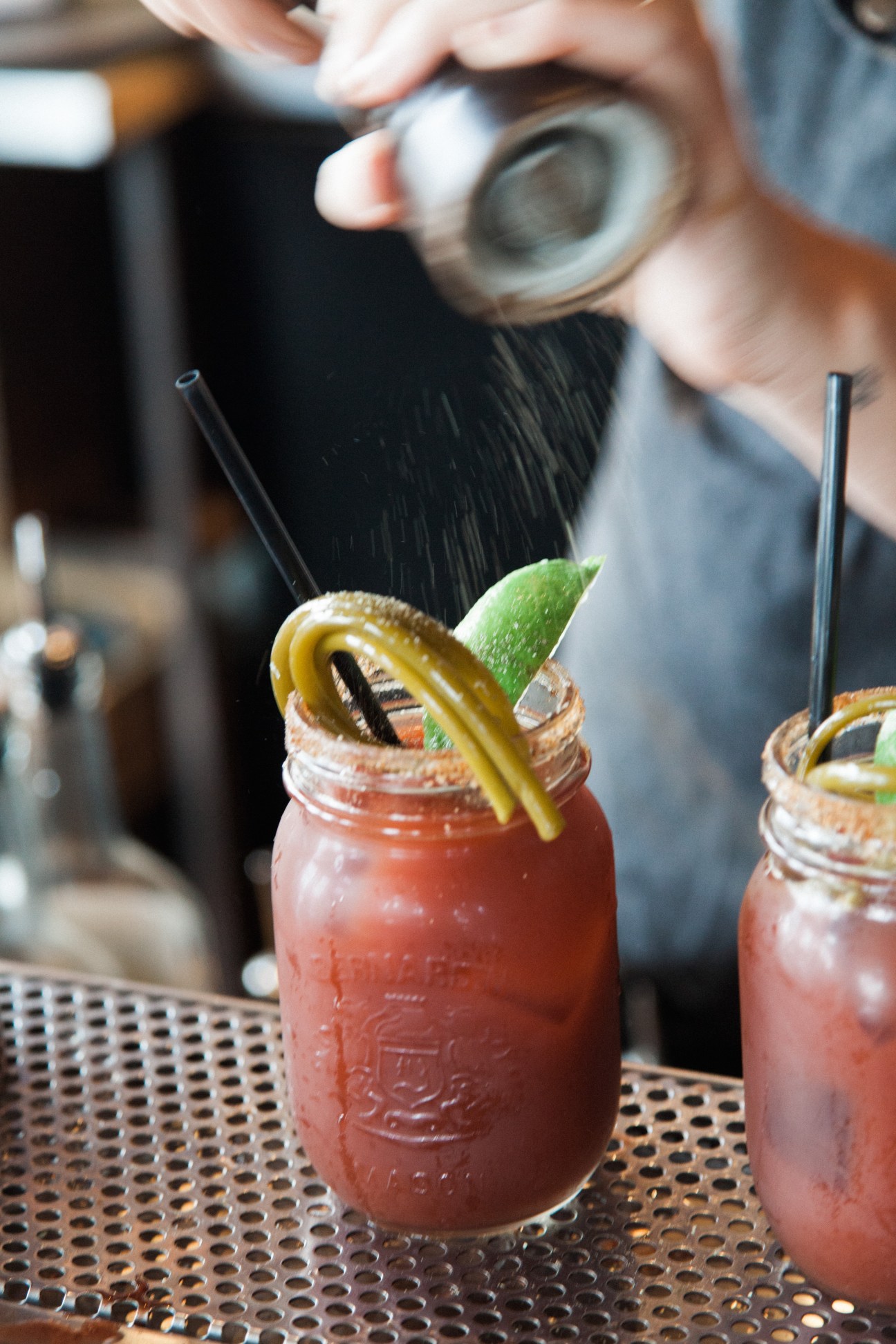 Bartender seasoning red cocktails in mason jars with lime garnish at Wolf in the Fog