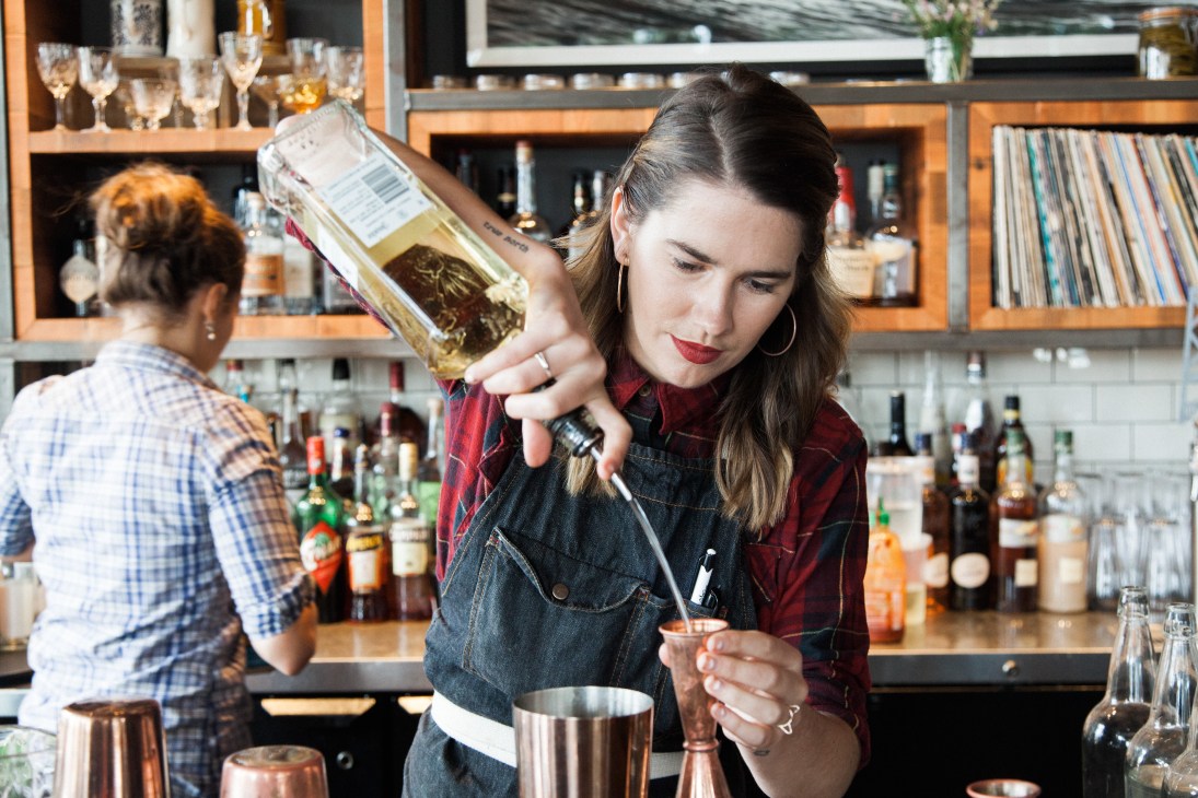 Bartender in denim apron pouring spirit into cocktail shaker at Wolf in the Fog restaurant