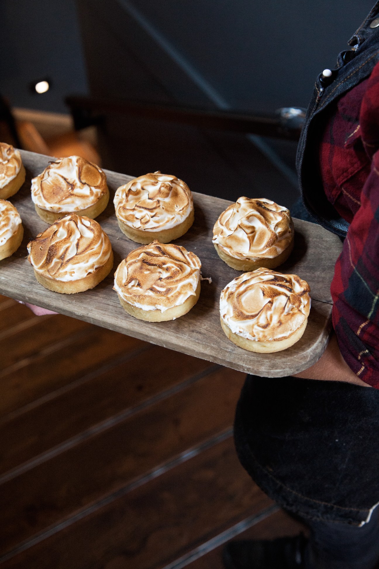 Small round pastries with golden-brown meringue tops arranged on a wooden serving board