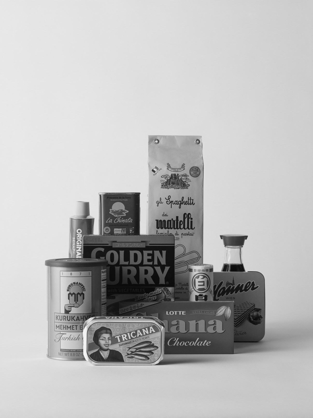 Black and white still life arrangement of various food and beverage products and packages stacked together