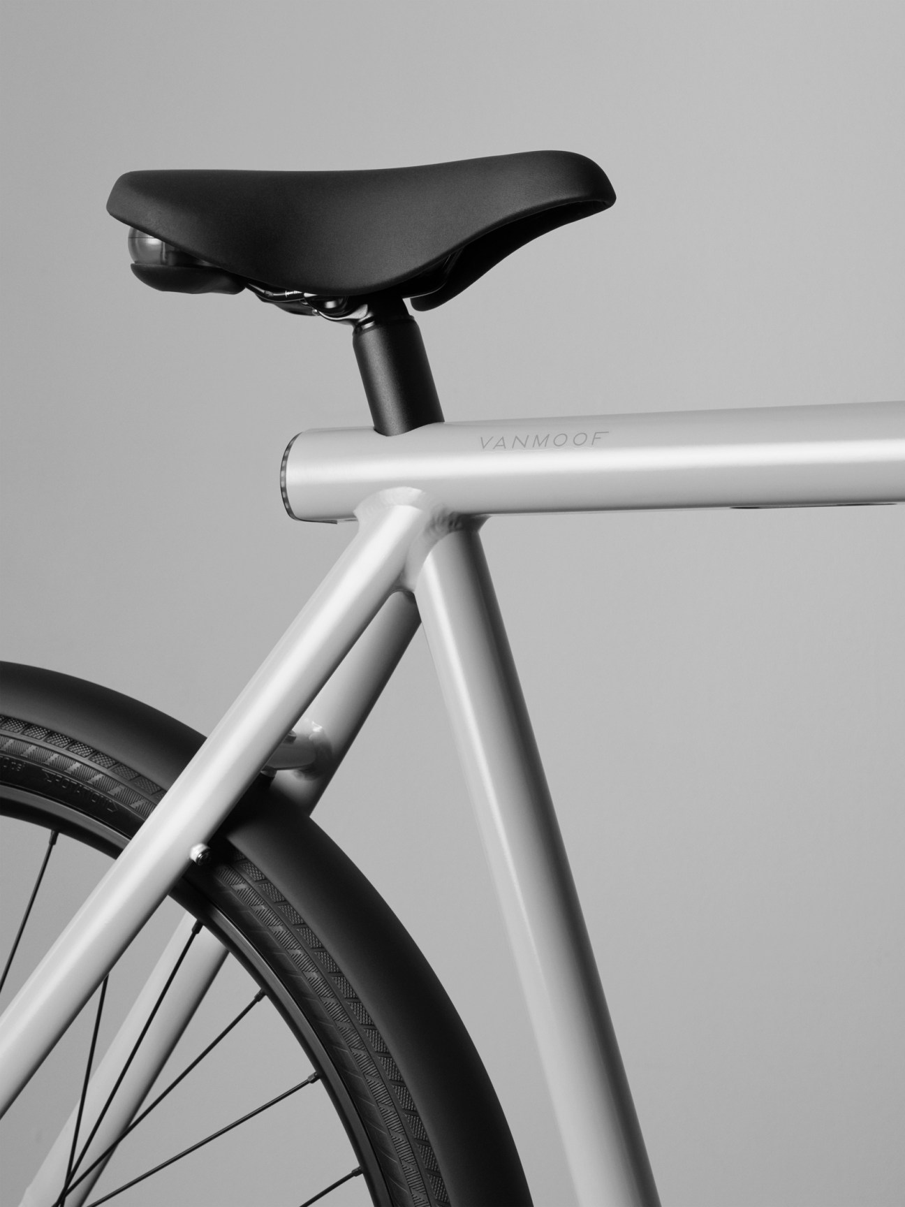 Close-up detail of white bicycle frame showing VanMoof branding on top tube with black seat and wheel visible