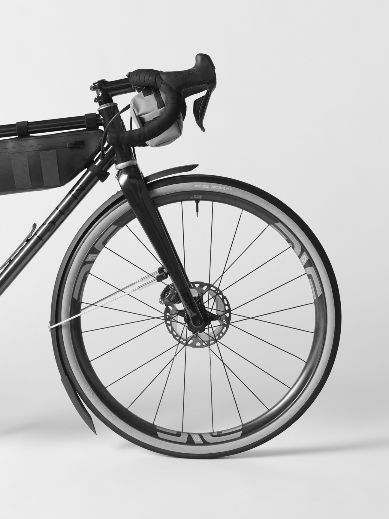 Close-up of a black bicycle wheel with disc brake and drop handlebars against white background