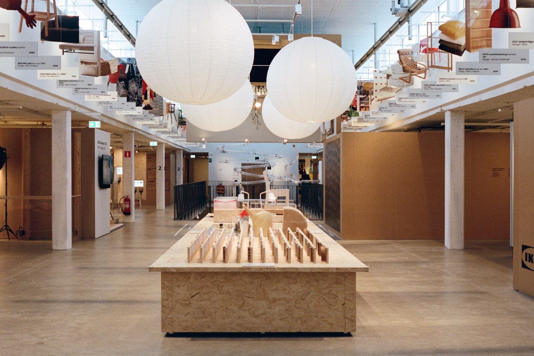 Interior of the Ikea Museum showing a product timeline display with wooden components and suspended circular light fixtures.
