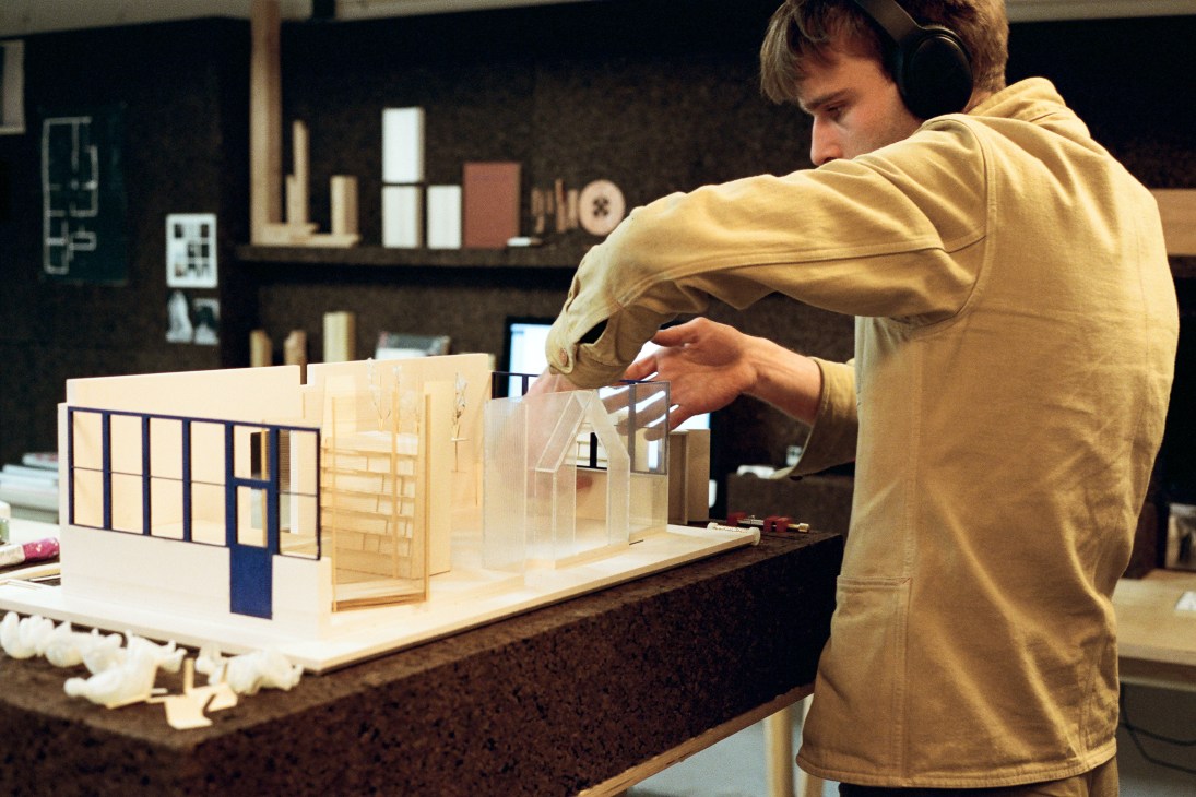 Person in yellow hoodie wearing headphones examines an architectural model at Space10.
