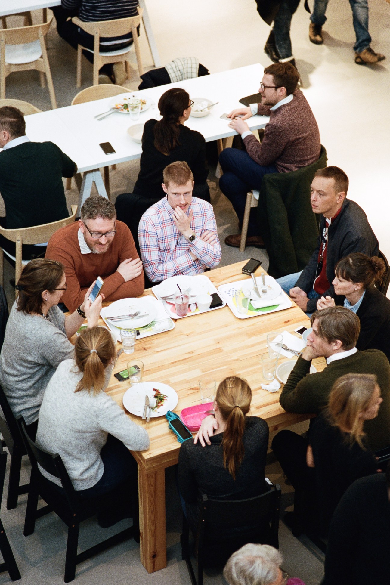 Overhead view of diverse group of people seated at wooden tables during lunch at the Democratic Design Centre.