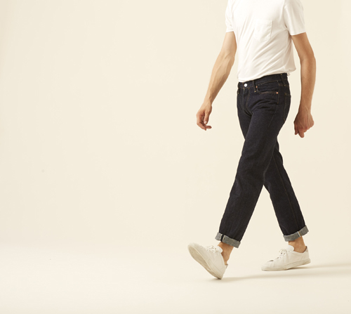 Man wearing 66 jeans by Denime in dark indigo with rolled cuffs and white sneakers