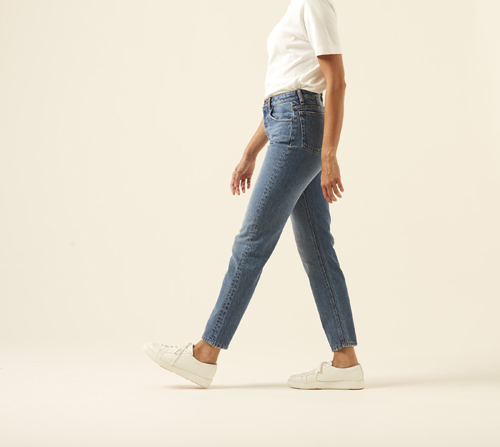 Person wearing AMI fit jeans in dark wash with white t-shirt and sneakers against cream background