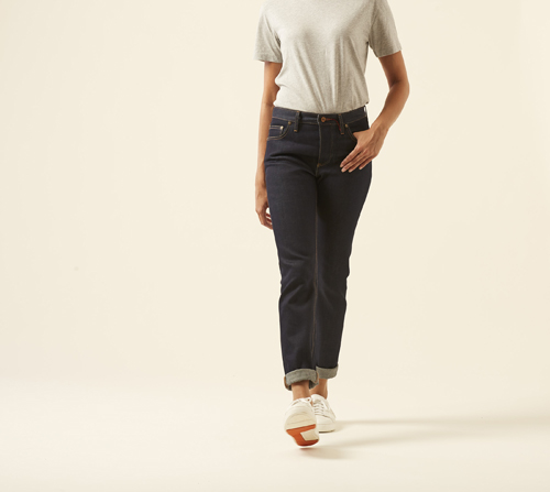 Woman wearing The Coda jeans by Hiut Denim Co in dark indigo with cuffed ankles and white sneakers.