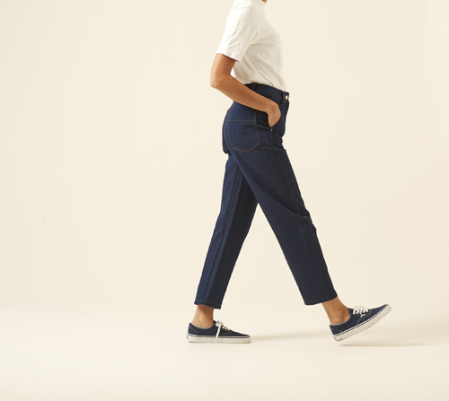 Person wearing Lemaire twisted pants in dark navy with white t-shirt and navy sneakers, side profile walking stance.