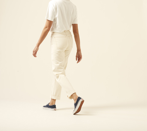 Person wearing white shirt and cream straight-leg jeans by Arket with rolled ankles and navy sneakers.