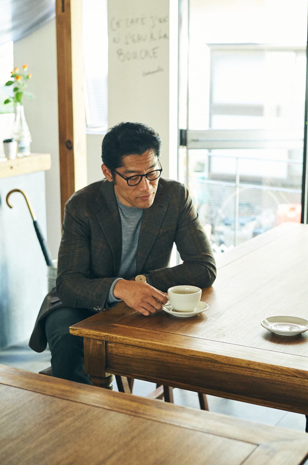 Man wearing Orazio Luciano jacket and Brooks Brothers jumper sits at wooden table with tea cup.