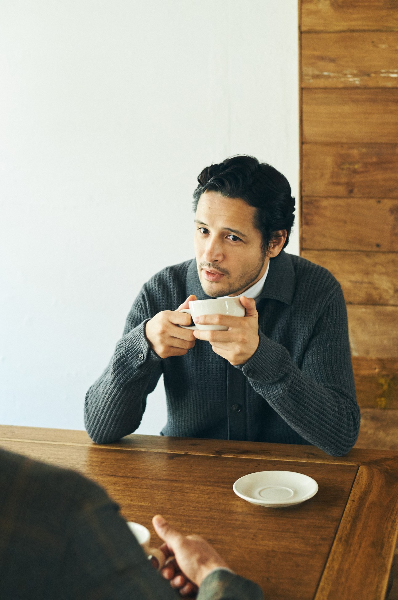 Man in Ermenegildo Zegna cardigan and Circolo 1901 rollneck holding a cup at wooden table.